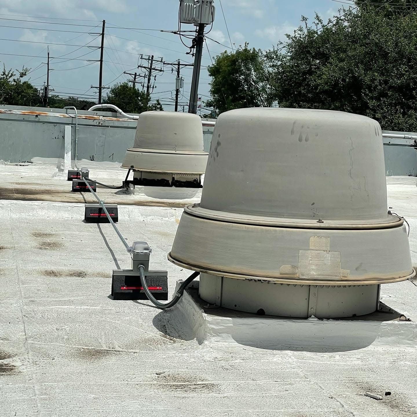 Two large, weathered roof vents on a flat rooftop with wiring and antennas.